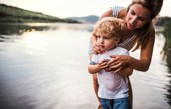 A young mother with a toddler boy outdoors by the river in summer. Copy space.