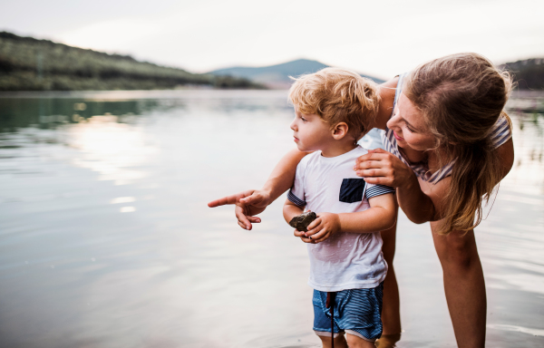 A young mother with a toddler boy outdoors by the river in summer. Copy space.