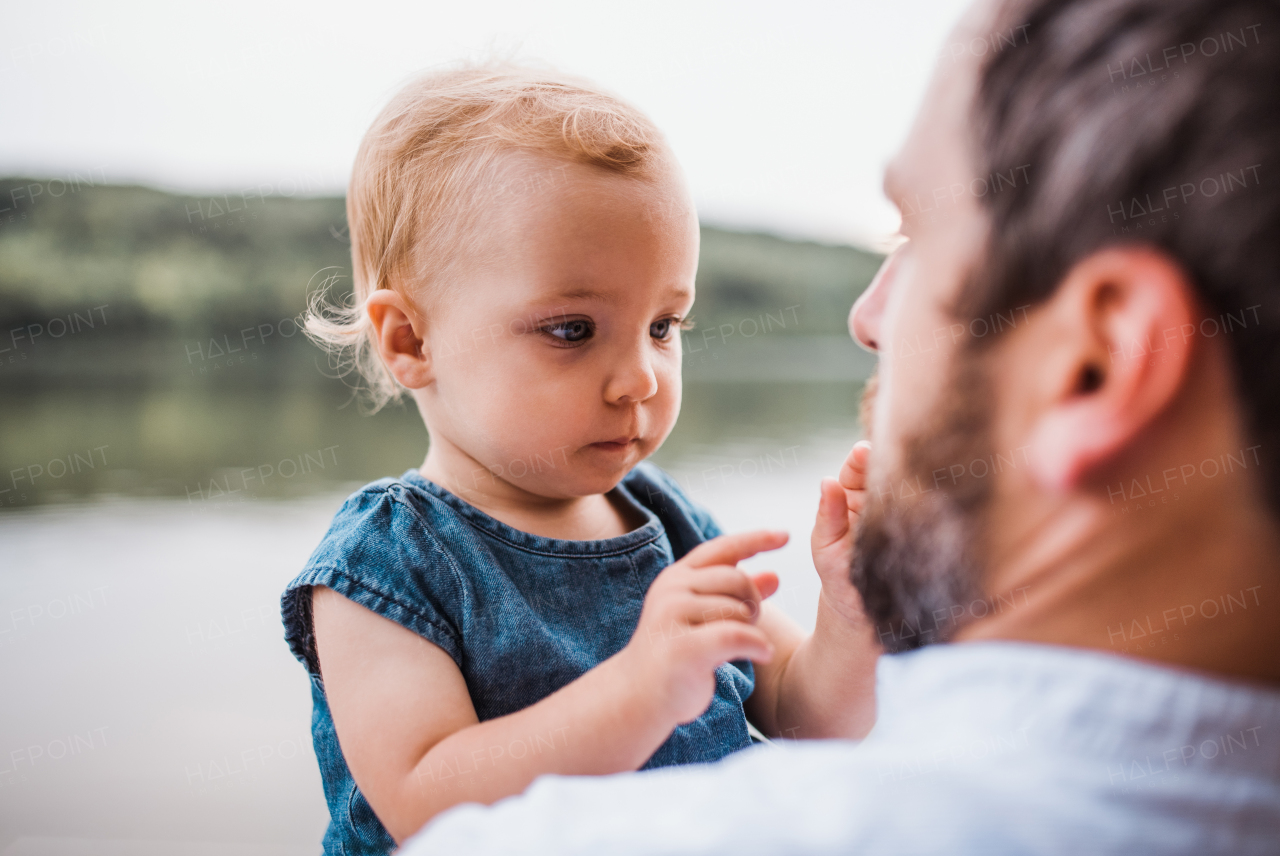 A mature father with a toddler girl outdoors by the river in summer.