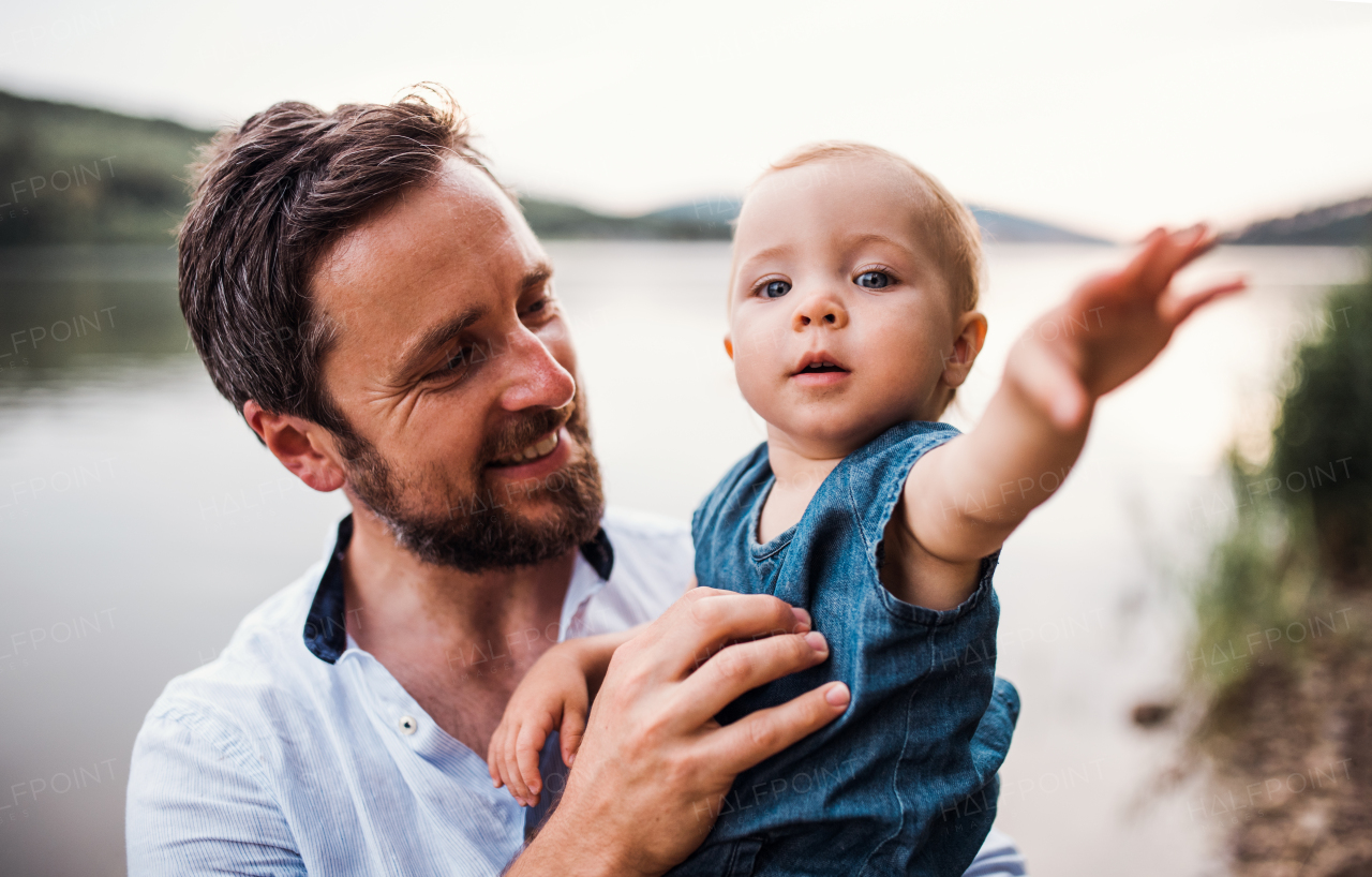 A mature father with a toddler girl outdoors by the river in summer.