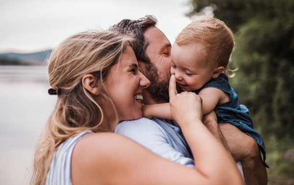 A young family with a toddler girl outdoors by the river in summer, having fun.