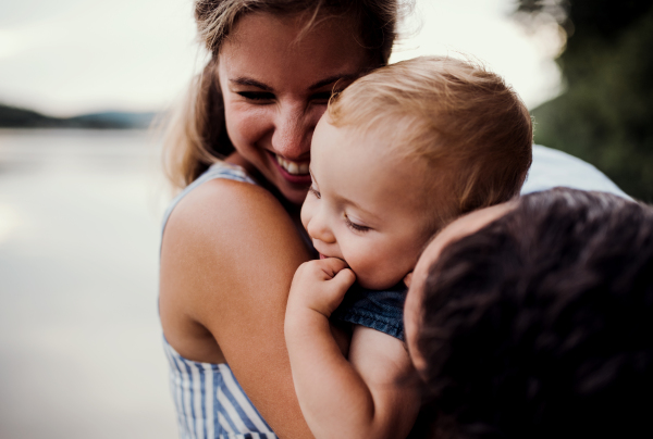 A young family with a toddler girl outdoors by the river in summer, having fun.