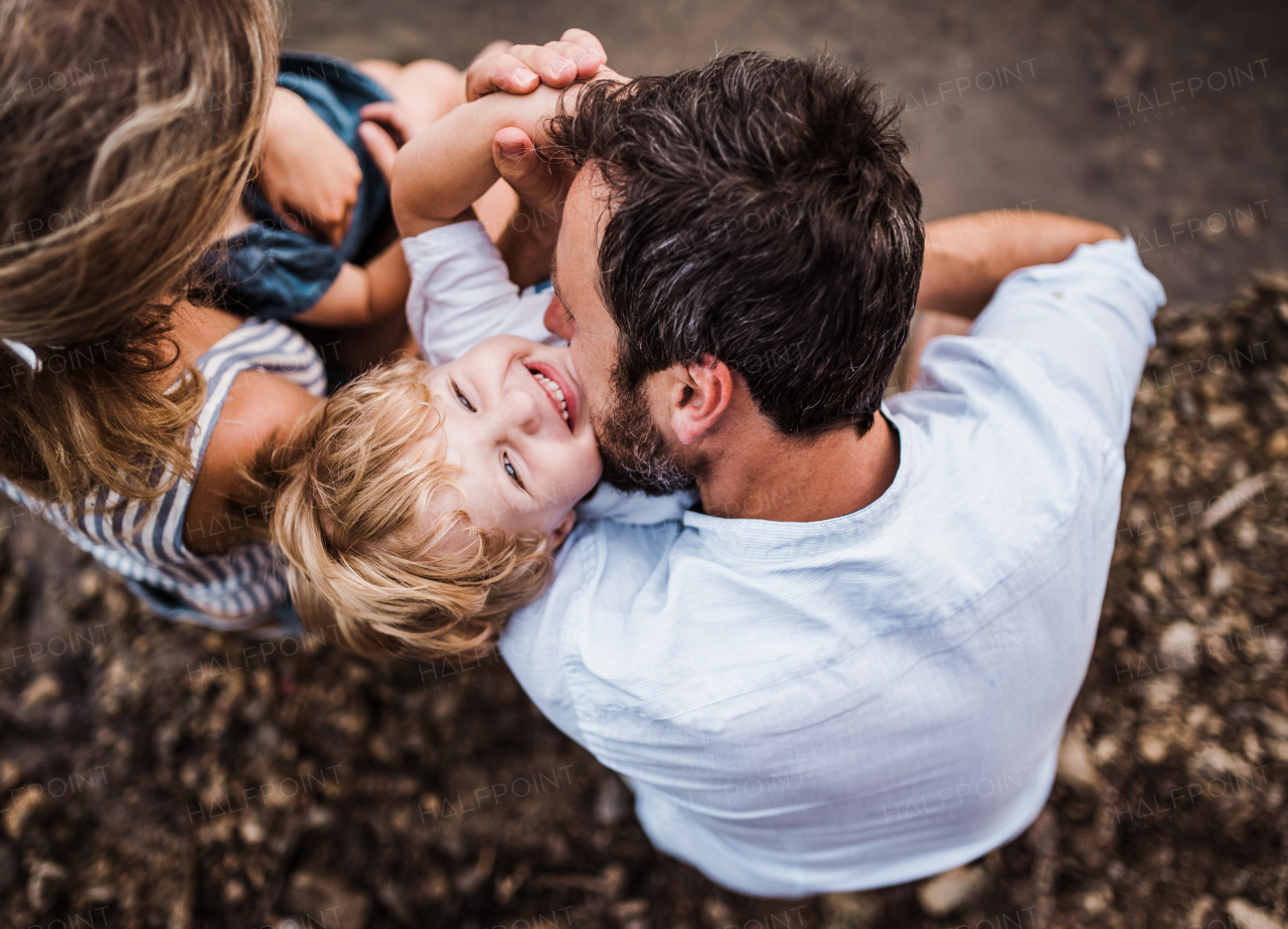 A top view of young family with two toddler children spending time outdoors by the river in summer, having fun.