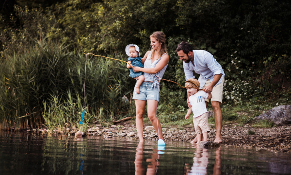 A young family with two toddler children spending time outdoors by the river in summer.