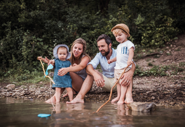 A young family with two toddler children spending time outdoors by the river in summer.