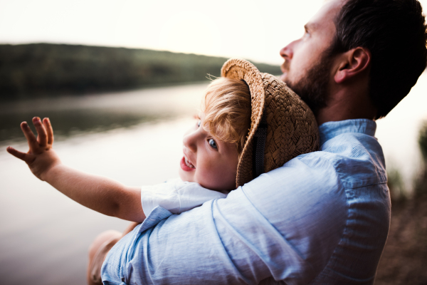 A mature father with a toddler boy outdoors by the river in summer.