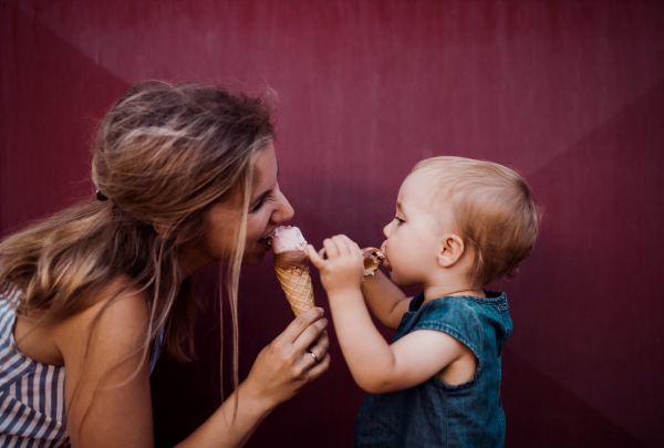 A young mother with small toddler girl outdoors in summer, eating ice cream.