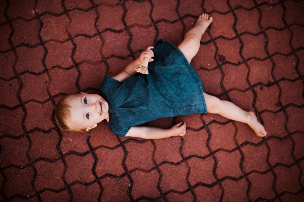 A top view of cute small toddler lgirl lying outdoors in summer, eating ice cream.