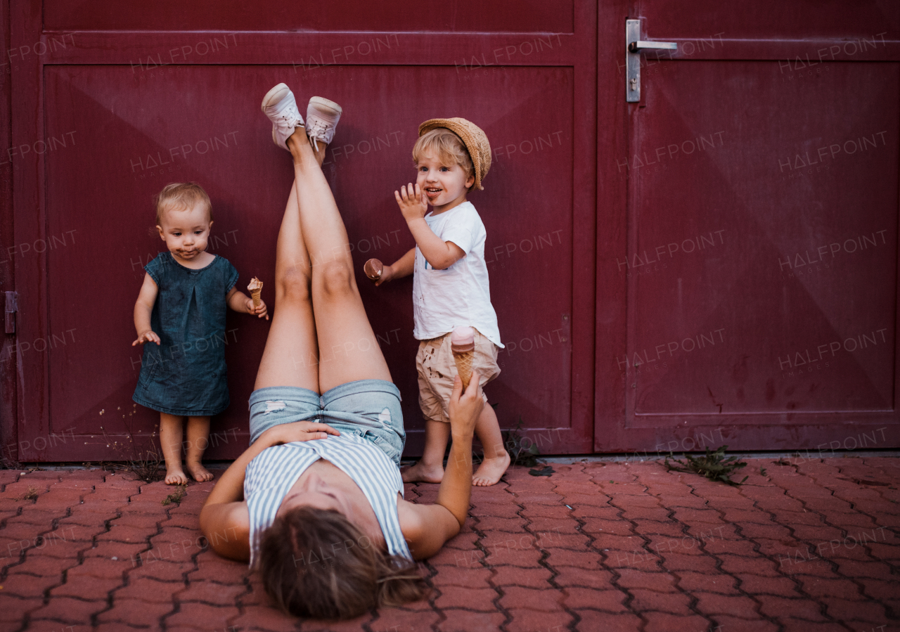 A young unrecognizable mother with two toddler children outdoors in summer, eating ice cream.