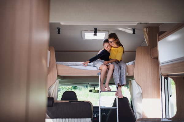 Happy small girls sisters sittining on bed indoors in caravan, family holiday trip.