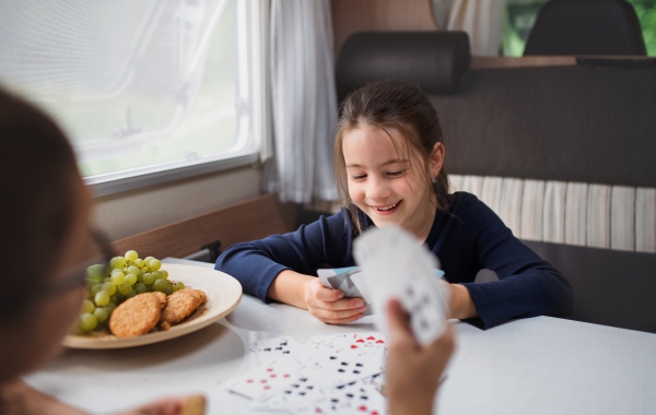 Happy small girls playing cards indoors in caravan, family holiday trip.