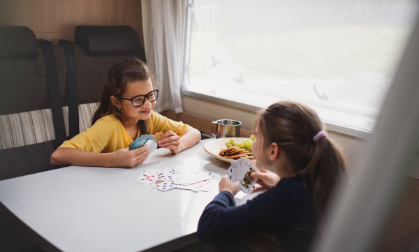 Happy small girls playing cards indoors in caravan, family holiday trip.