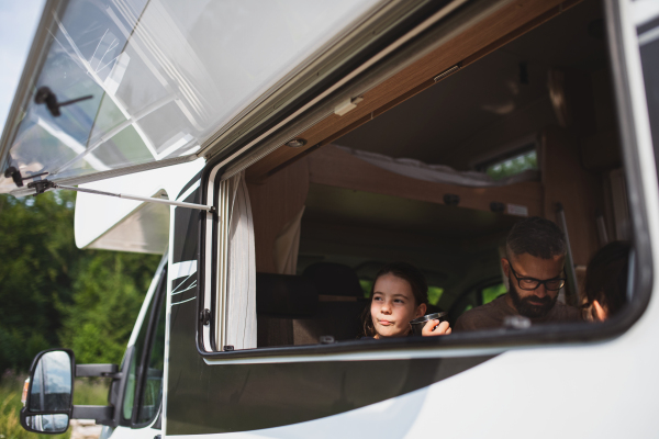 A happy small girl with father sitting in caravan, family holiday trip.