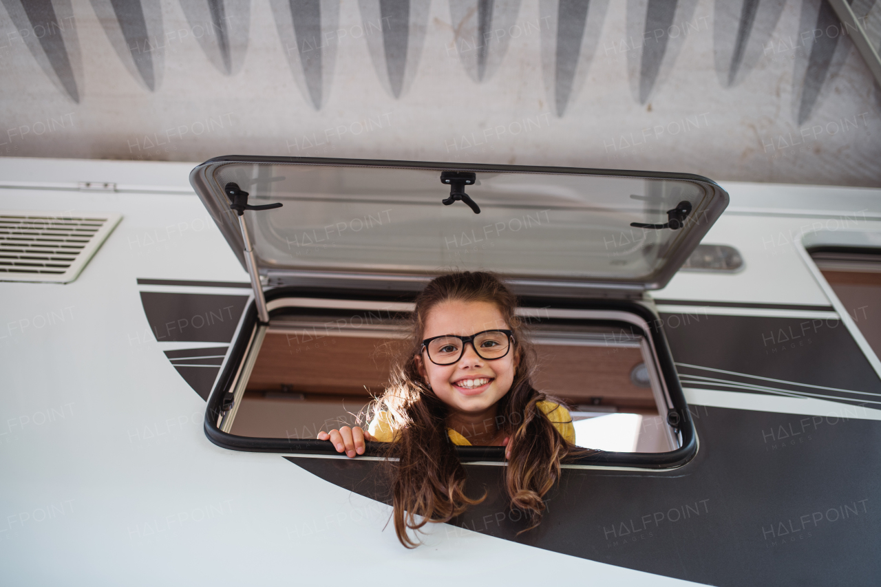 A happy small girl looking out through caravan window and looking at camera, family holiday trip.