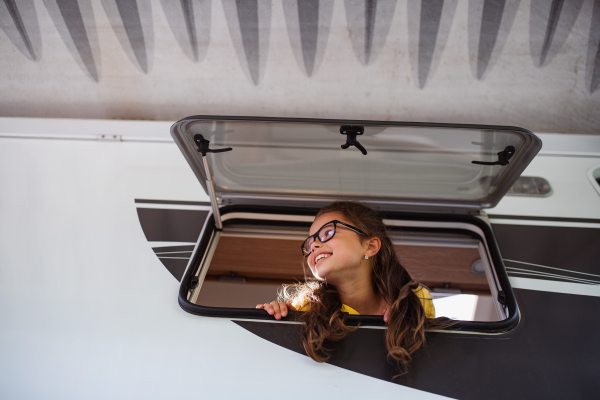 A happy small girl looking out through caravan window, family holiday trip.