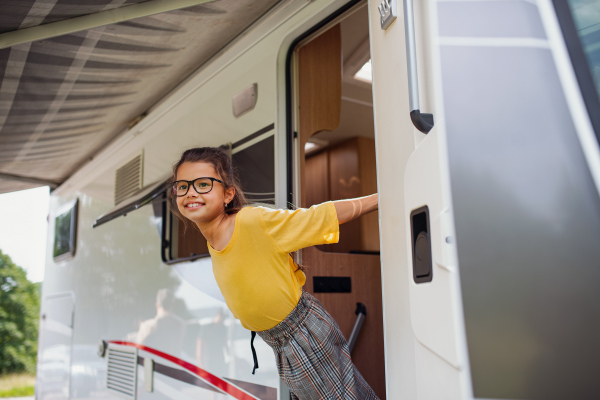 A happy small girl standing by caravan door, family holiday trip.