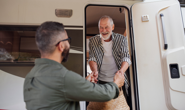 A mature man with senior father unpacking by car outdoors, caravan holiday trip.