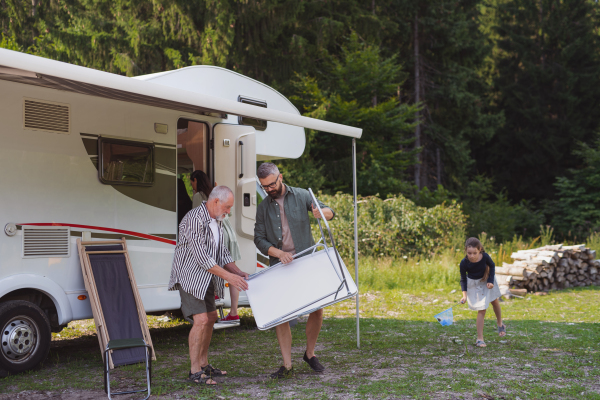 Happy multi-generation family unpacking and talking by car, caravan holiday trip.