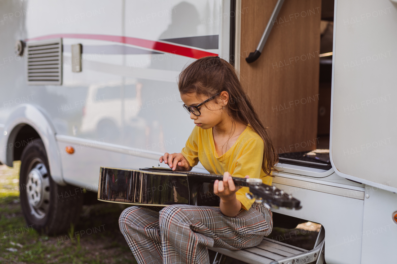 Happy small girl with guitar playing by caravan, family holiday trip.