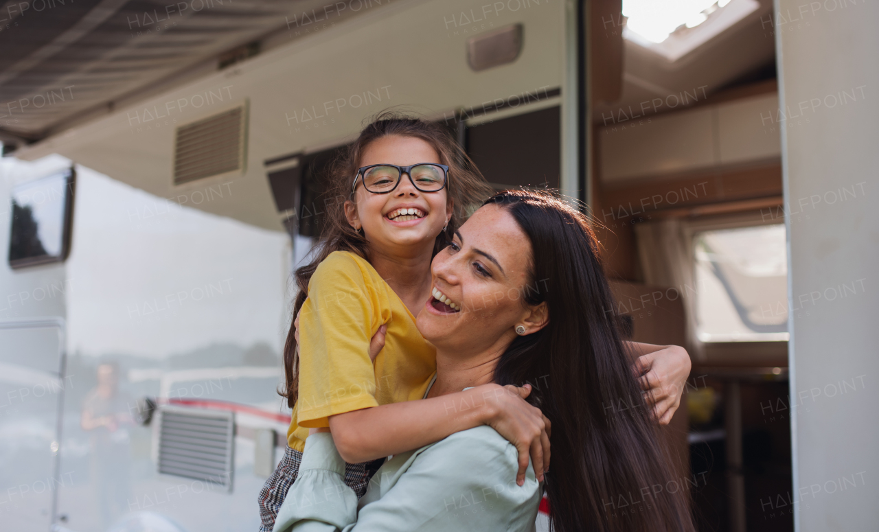 A mother hugging daughter by car outdoors in campsite at dusk, caravan family holiday trip.