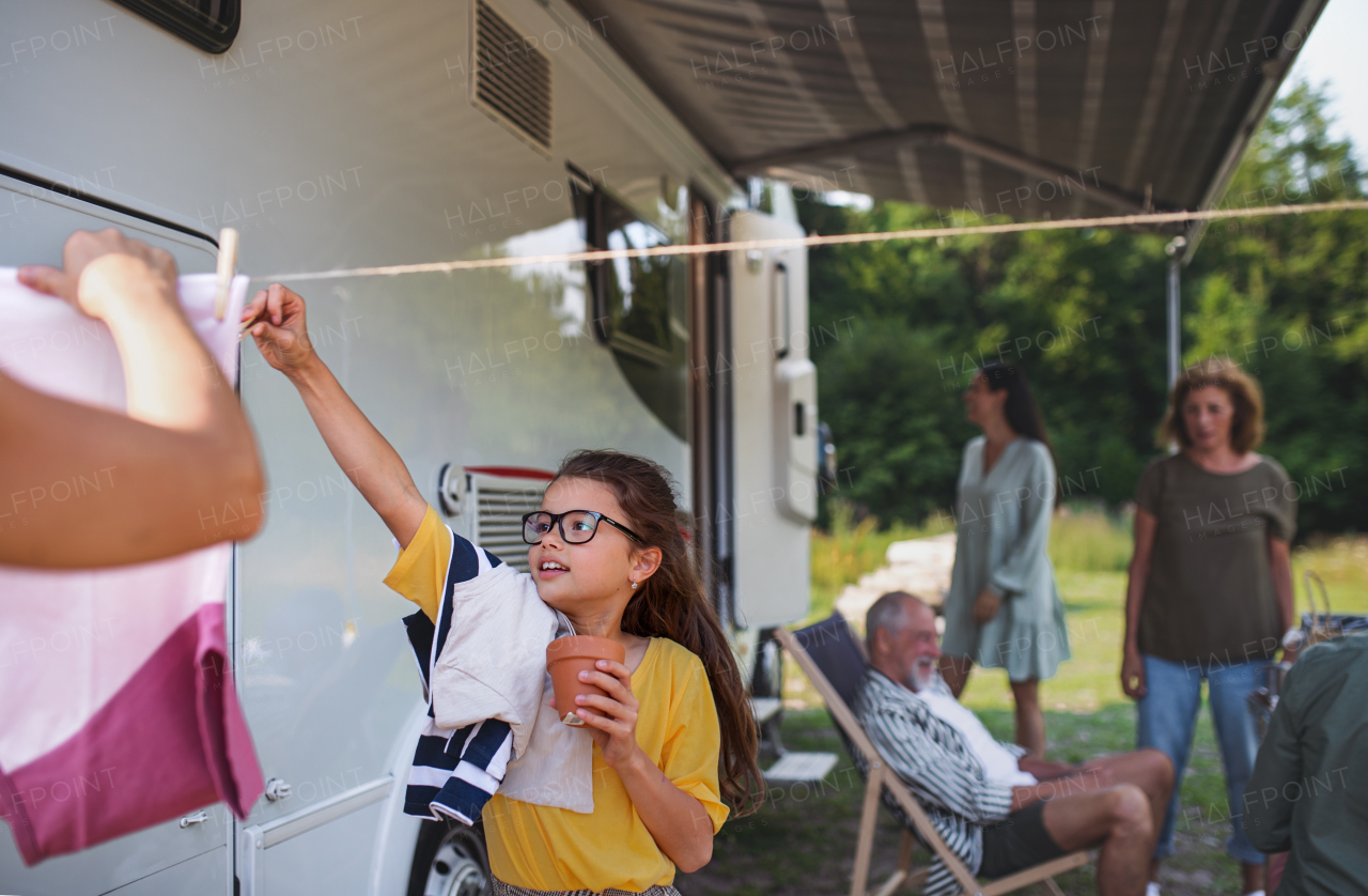 An unrecognizable father with daughter hanging clothes by car outdoors in campsite, caravan family holiday trip.