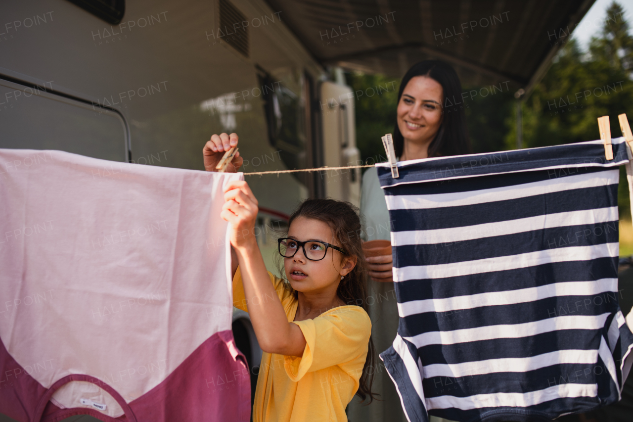 A mother with daughter hanging clothes by car outdoors in campsite, caravan family holiday trip.