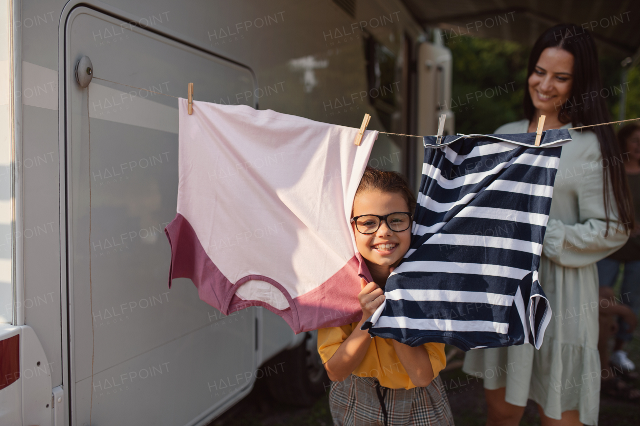 A mother with daughter hanging clothes by car outdoors in campsite, caravan family holiday trip.