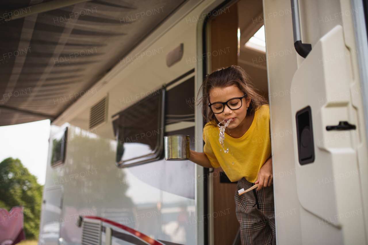 A happy small girl brushing teeth by caravan, family holiday trip.