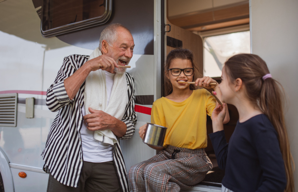 Happy small girls with a grandfather brushing teeth by caravan, family holiday trip.