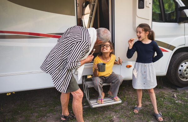 Happy small girls with a grandfather brushing teeth by caravan, family holiday trip.