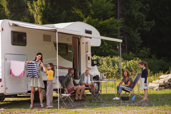 A mother with daughter hanging clothes by car outdoors in campsite, caravan family holiday trip.