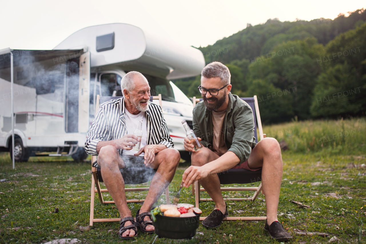 A mature man with senior father talking at campsite outdoors, barbecue on caravan holiday trip.