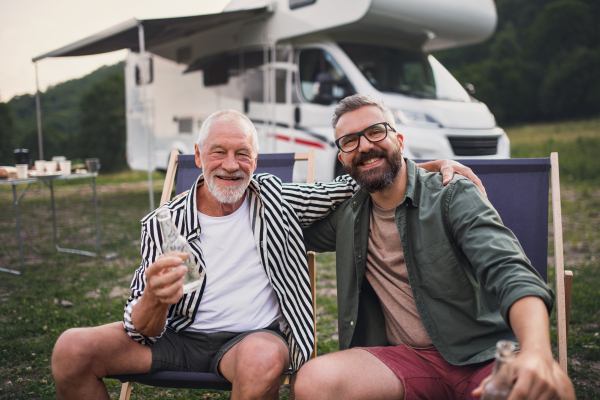 A mature man with senior father looking at camera at campsite outdoors, barbecue on caravan holiday trip.