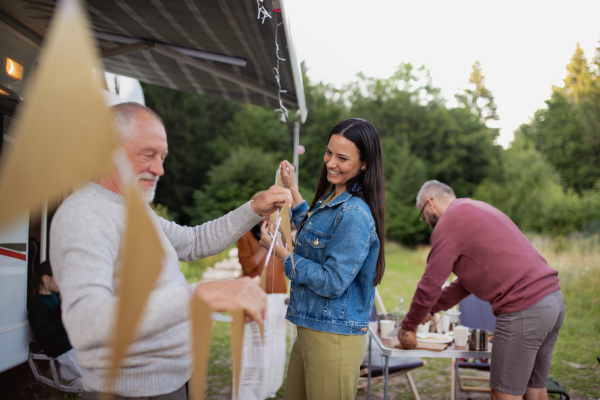 Happy multi-generation family preparing party by car outdoors in campsite, caravan holiday trip.