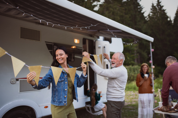 Happy multi-generation family preparing party by car outdoors in campsite, caravan holiday trip.