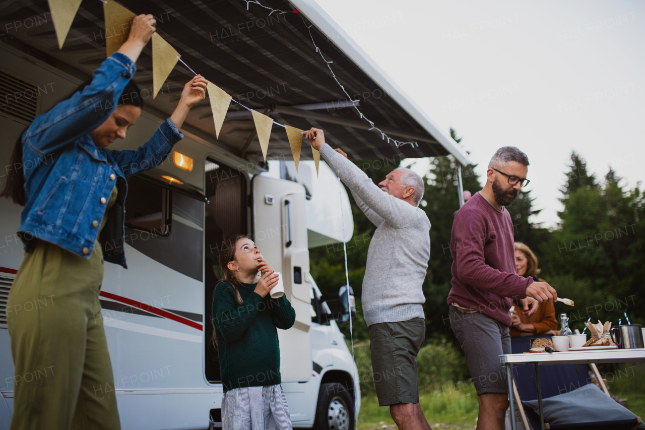 Happy multi-generation family preparing party by car outdoors in campsite, caravan holiday trip.