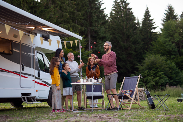 A multi-generation family standing and having fun outdoors by car, caravan holiday trip.