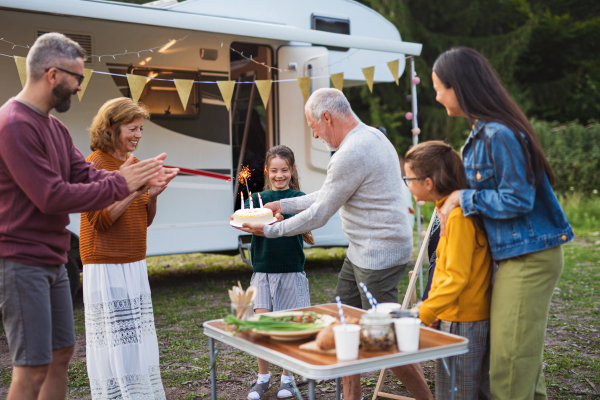 A multi-generation family celebrating birthday outdoors at campsite, caravan holiday trip.