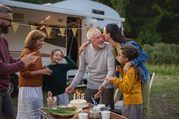 A senior man celebrating birthday outdoors at campsite, multi-generation family caravan holiday trip.