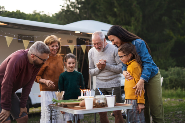 A senior man celebrating birthday outdoors at campsite, multi-generation family caravan holiday trip.