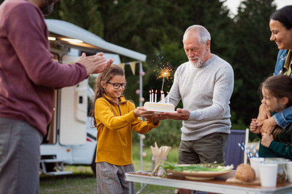 A multi-generation family celebrating birthday outdoors at campsite, caravan holiday trip.