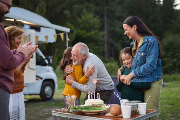 A multi-generation family celebrating birthday outdoors at campsite, caravan holiday trip.