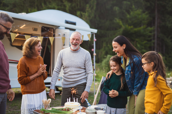 A multi-generation family celebrating birthday outdoors at campsite, caravan holiday trip.