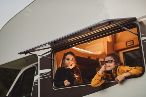 Happy small girls looking out through caravan window in the evening, a family holiday trip.