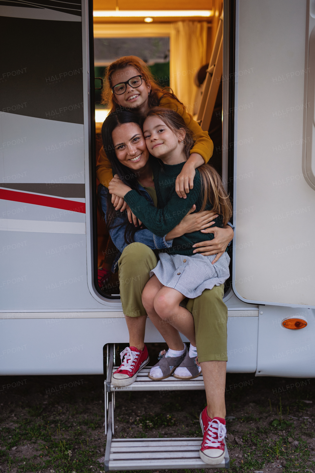 Happy mother with daughters by car outdoors in campsite at dusk, caravan family holiday trip.