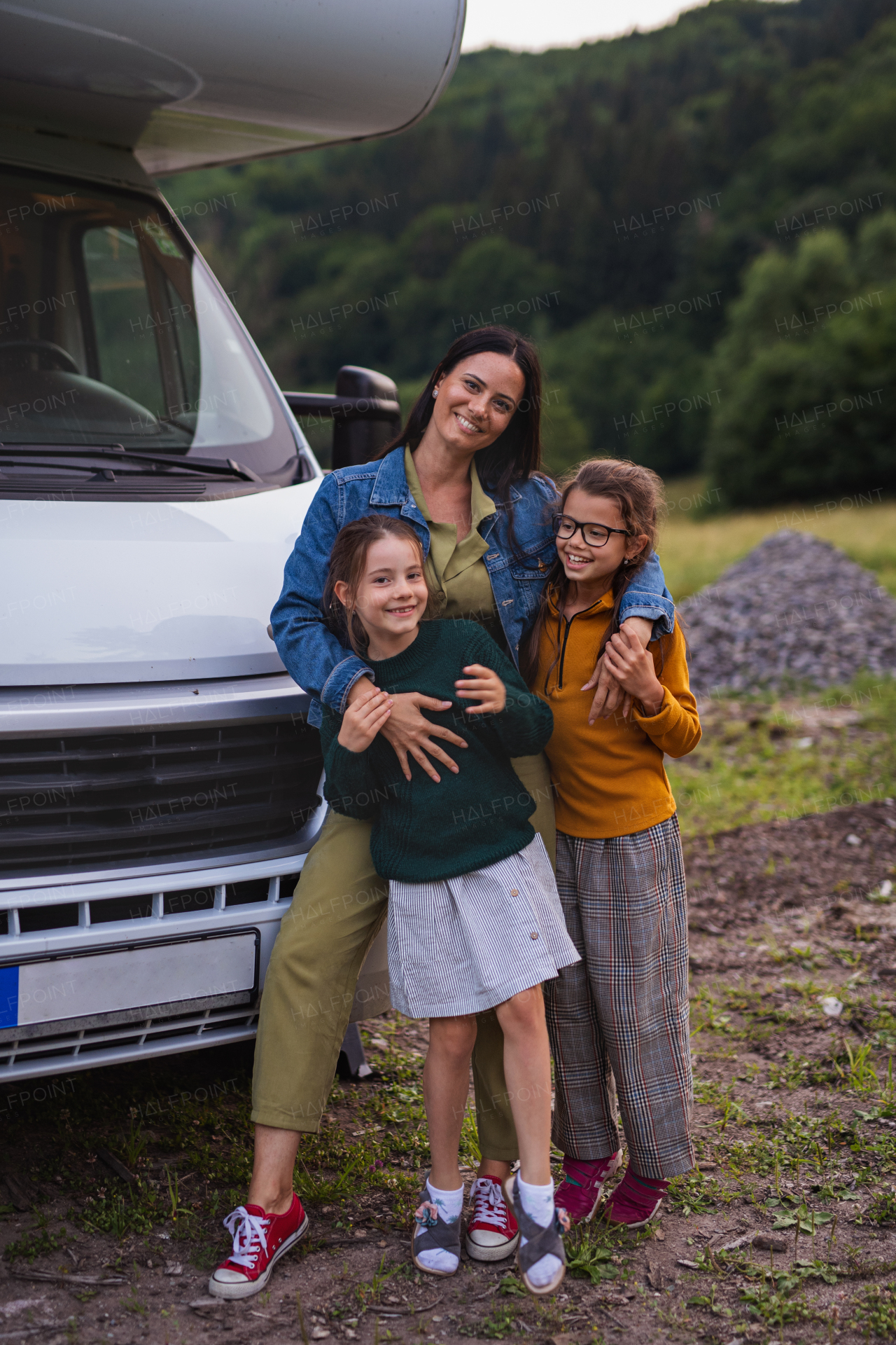 Happy mother with daughters standing by car outdoors in campsite at dusk, caravan family holiday trip.