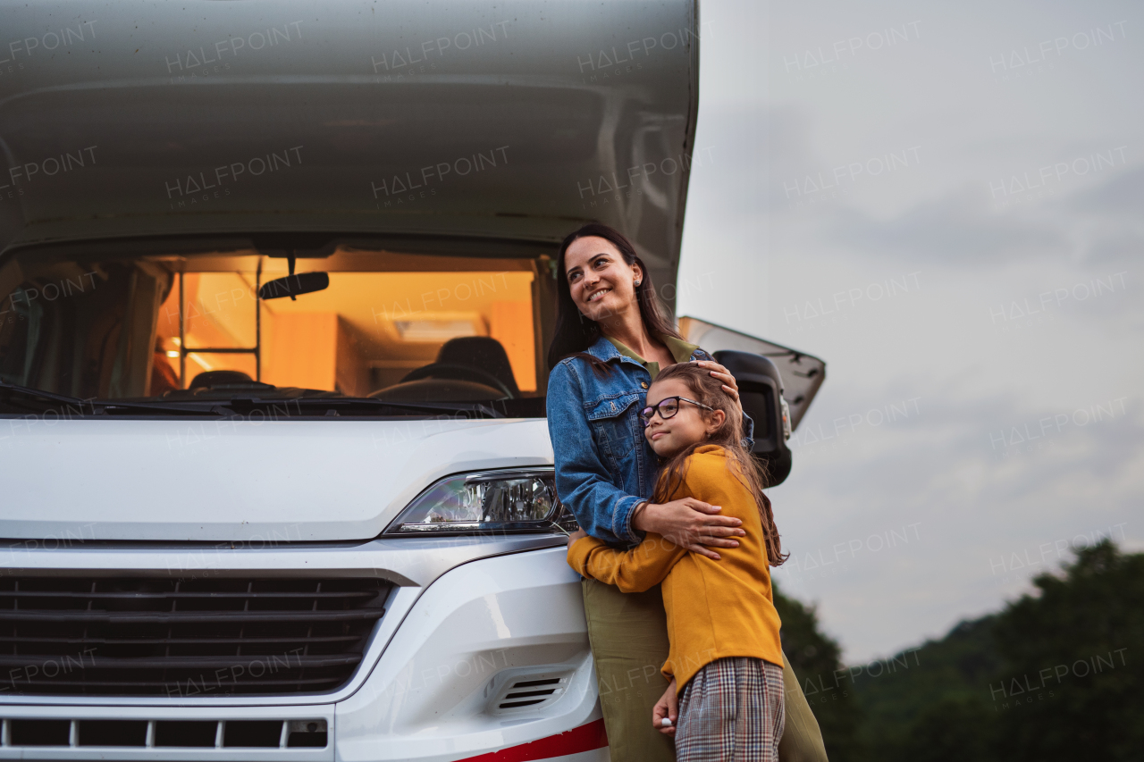 Happy mother with daughter standing by car outdoors in campsite at dusk, caravan family holiday trip.