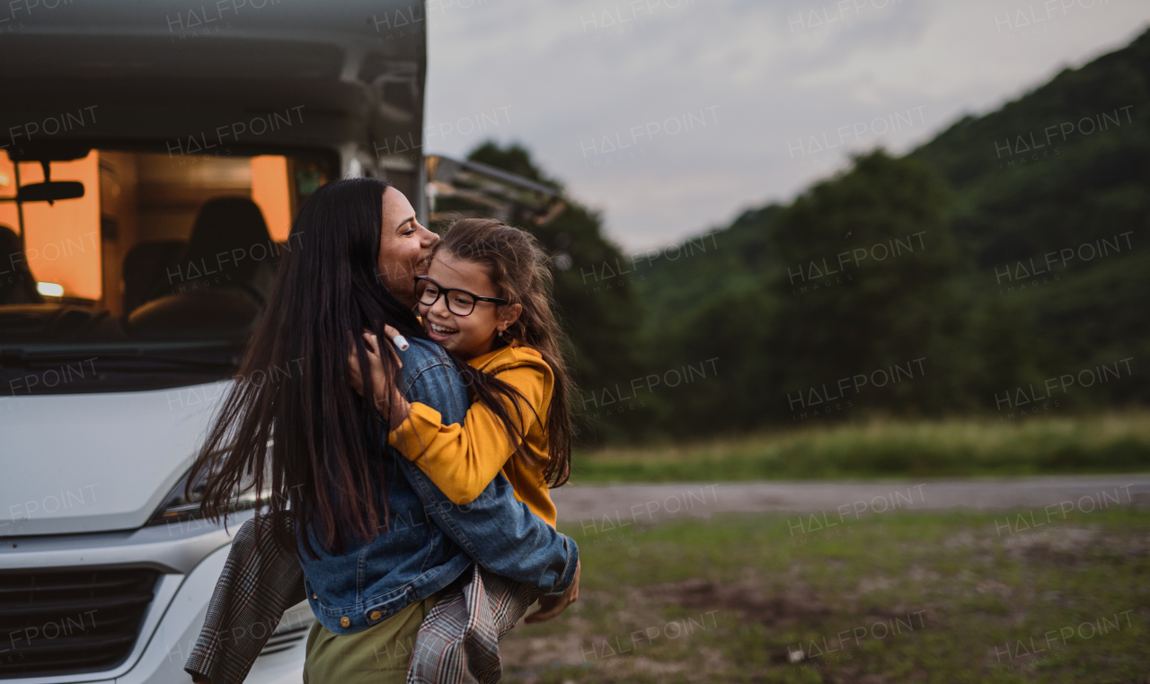 A happy mother with small daughter hugging by car outdoors in campsite at dusk, caravan family holiday trip.