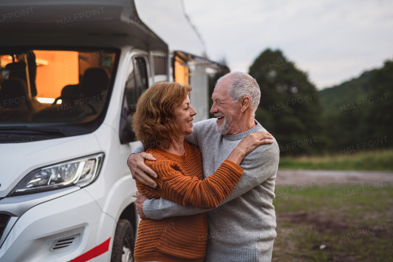 A senior couple standing and hugging outdoors at dusk, caravan holiday trip.