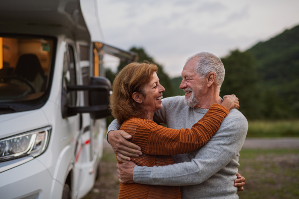 A senior couple standing and hugging outdoors at dusk, caravan holiday trip.